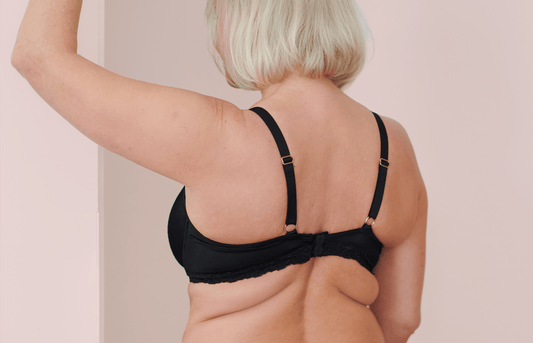 Woman wearing a black bra with her back turned towards the camera showing the bra clasps and back straps.